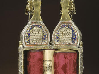 Ornately decorated cylindrical case with Hebrew writing on top and scroll inside; closed cylindrical case with ornate decoration.