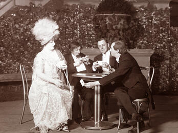 Hokey Pokey Photograph of three men and a woman in large hat seated at a table playing cards.