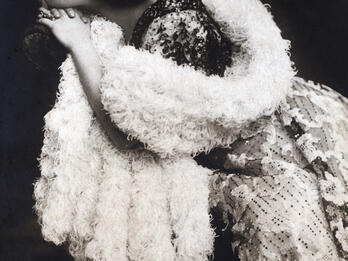 Alla Nazimova as Hedda Gabler Photograph of woman in boa sitting on chair and looking to the side.