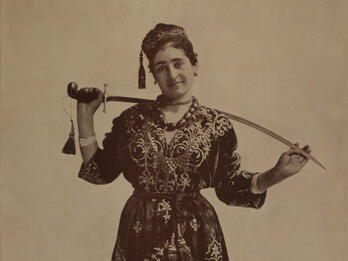 Photograph of figure holding sword behind her neck.