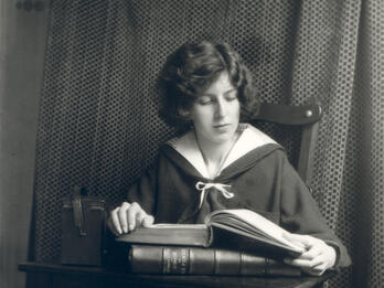 Photograph of figure seated at desk reading a book.