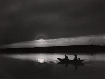 Photograph of two figures in a boat at sunset.