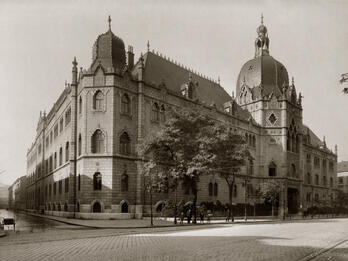 Photograph of brick building on street corner with ornate roof finials and domed roofs.