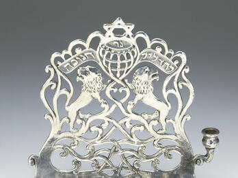 Hanukkah Lamp Eight-branched candelabrum with backplate with lions, a Hebrew inscription, Stars of David, and a scalloped top edge.