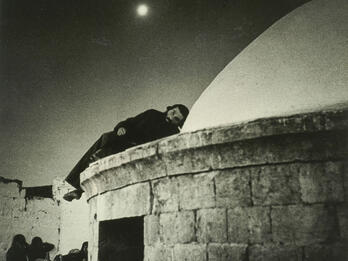 Night of Meron Photograph of man lying on domed roof of stone building.