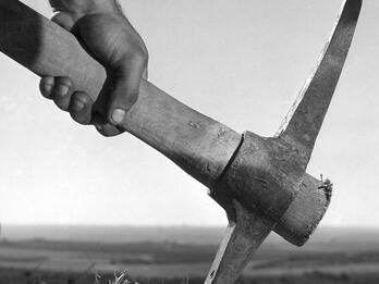 Land Is Life Photograph of a hand holding a garden pick with field in background.