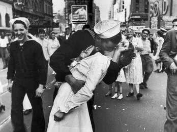 V-J Day in Times Square. August 14, 1945 Photograph of sailor grabbing and kissing a woman in a busy city street with people and buildings in background.