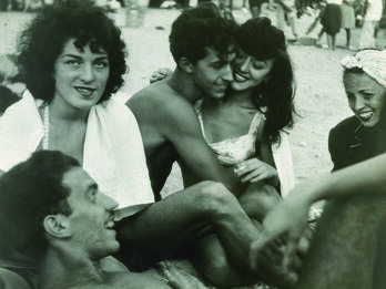 Coney Island Photograph of five people sitting closely together, with one lying down, in a circle on the beach.
