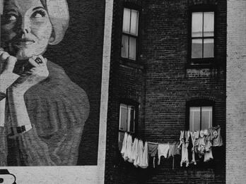 Lower Eastside Façade Photograph depicting painted advertisement of a woman on wall of brick building next to a clothesline on adjacent wall.