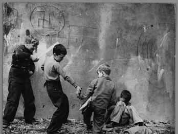 Yorkville Swastika Photograph of five young boys standing and sitting in various poses on crumbling foundation of a wall with swastika drawn on it. One boy points a flat wooden stick at another boy, who is giving a metal object to a seated boy.