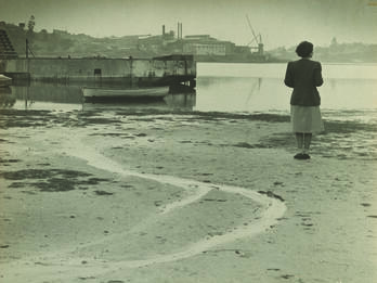 Self-Portrait, Parramatta River, Sydney Photograph of a woman standing on a wide beach and facing away from the viewer toward a river.