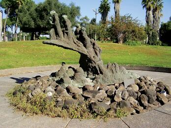 Holocaust and Rebirth (Kibbutz Nezer Sereni, Israel) Bronze monument set in a circular courtyard surrounded by grass and trees.