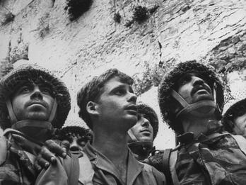 Paratroopers at the Western Wall, June 7, 1967 Photograph of three soldiers in uniform looking to their left standing in front of the Western Wall, with central soldier holding helmet in his hands.