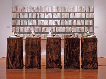 Installation featuring five podiums with an open book and reading light on top of each with open books on the wall behind. 
