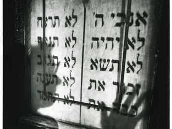 Shadow and Synagogue Photograph featuring shadow of a face and a hand over a wall with Hebrew text.
