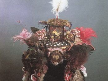 Assemblage of feathers, photographs, and figurines of humans and animals in a hat shape. 