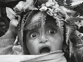 Good Friday Photograph of a wide-eyed baby with mouth open and ferns and flowers on their head.