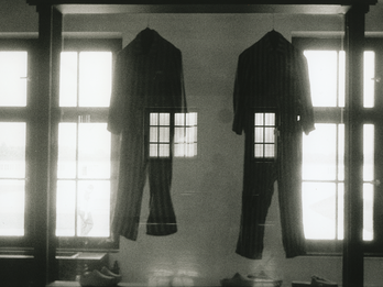 Photograph depicting two jumpsuits hanging between two large windows superimposed over an image of a human figure standing with their back turned. 