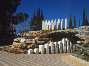 Monument featuring several stelae of different heights set along a rocky cave. 
