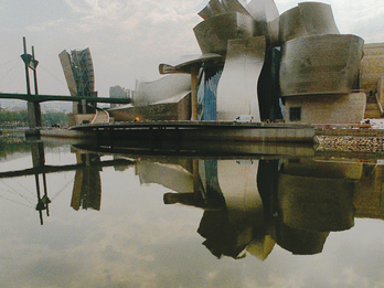Photograph of exterior building made up of cylindrical and ribbon shapes next to body of water. 