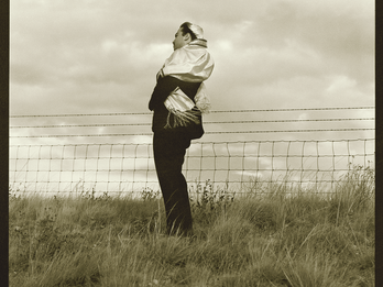 Home for the High Holy Days Full body photograph depicting man in kippah and prayer shawl standing in a field next to fence, facing to the side.
