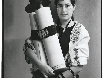 Dorothy A. Richman, Rabbinical Student, Jewish Theological Seminary Full body photograph of a person in glasses holding scroll with left arm wrapped in leather strap.