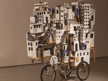 The Great Vehicle Mixed media work featuring stack of buildings on bicycle.