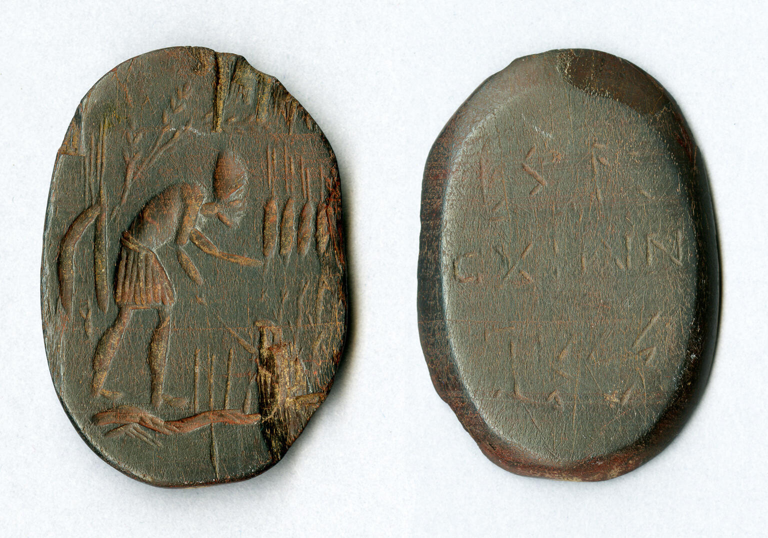 Two views of an ancient engraved oval stone: one side shows a standing, bent-over figure with an arm extended, while the other side displays several lines of inscribed text.
