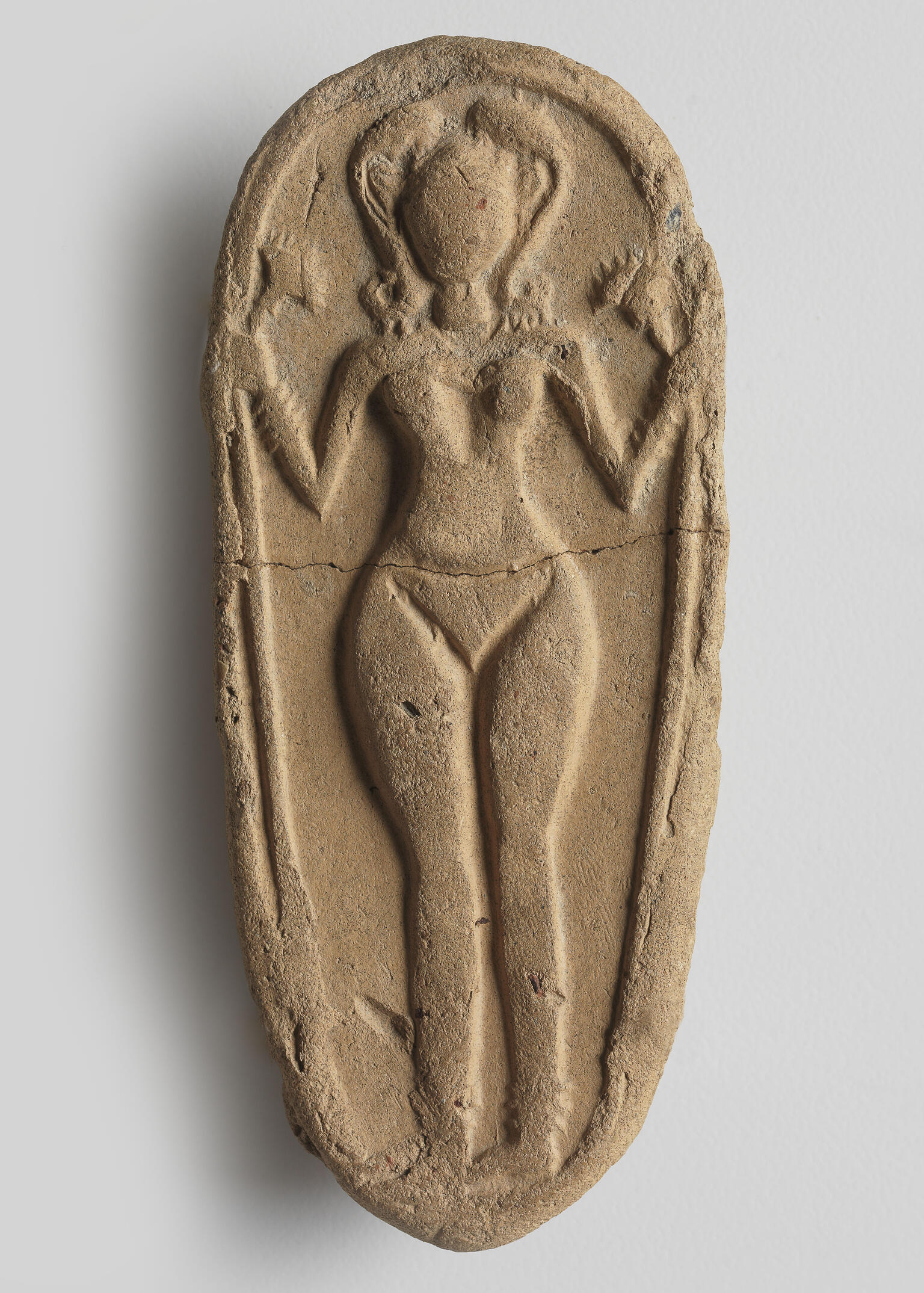 Oval clay piece with figurine of naked woman decorated with headdress, necklace, bracelets, and anklets, and holding a lotus flower. Oval clay piece with figurine of naked woman decorated with headdress, necklace, bracelets, and anklets, and holding a lotus flower.
