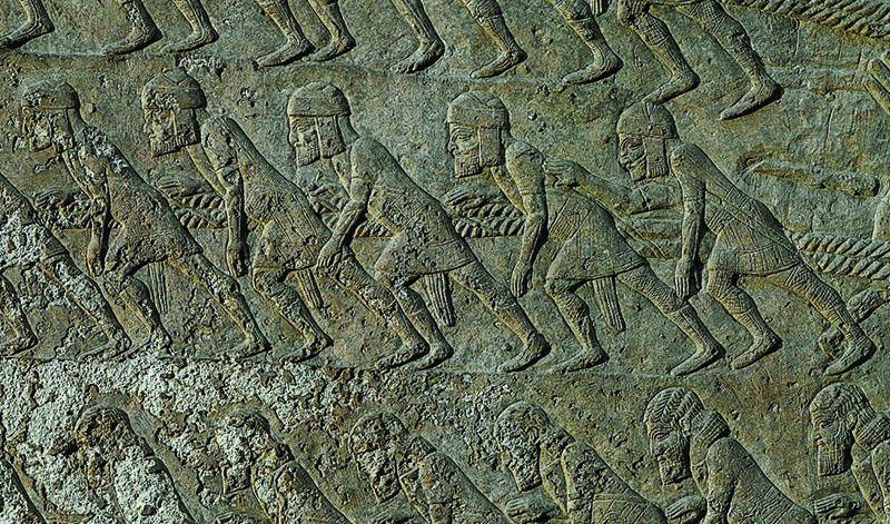 Wall relief showing workers wearing tunics, caps, and sashes, harnessed by shoulder straps to ropes and leaning forward.