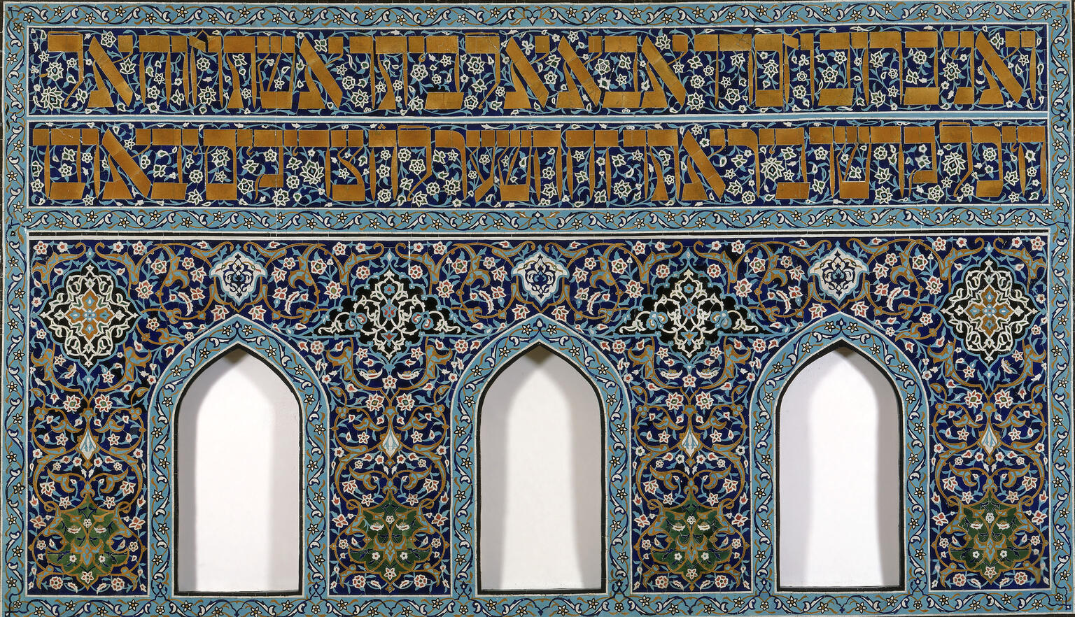 Faience-tile mosaic of floral designs throughout, two lines of Hebrew text at the top, and three niches at bottom.  