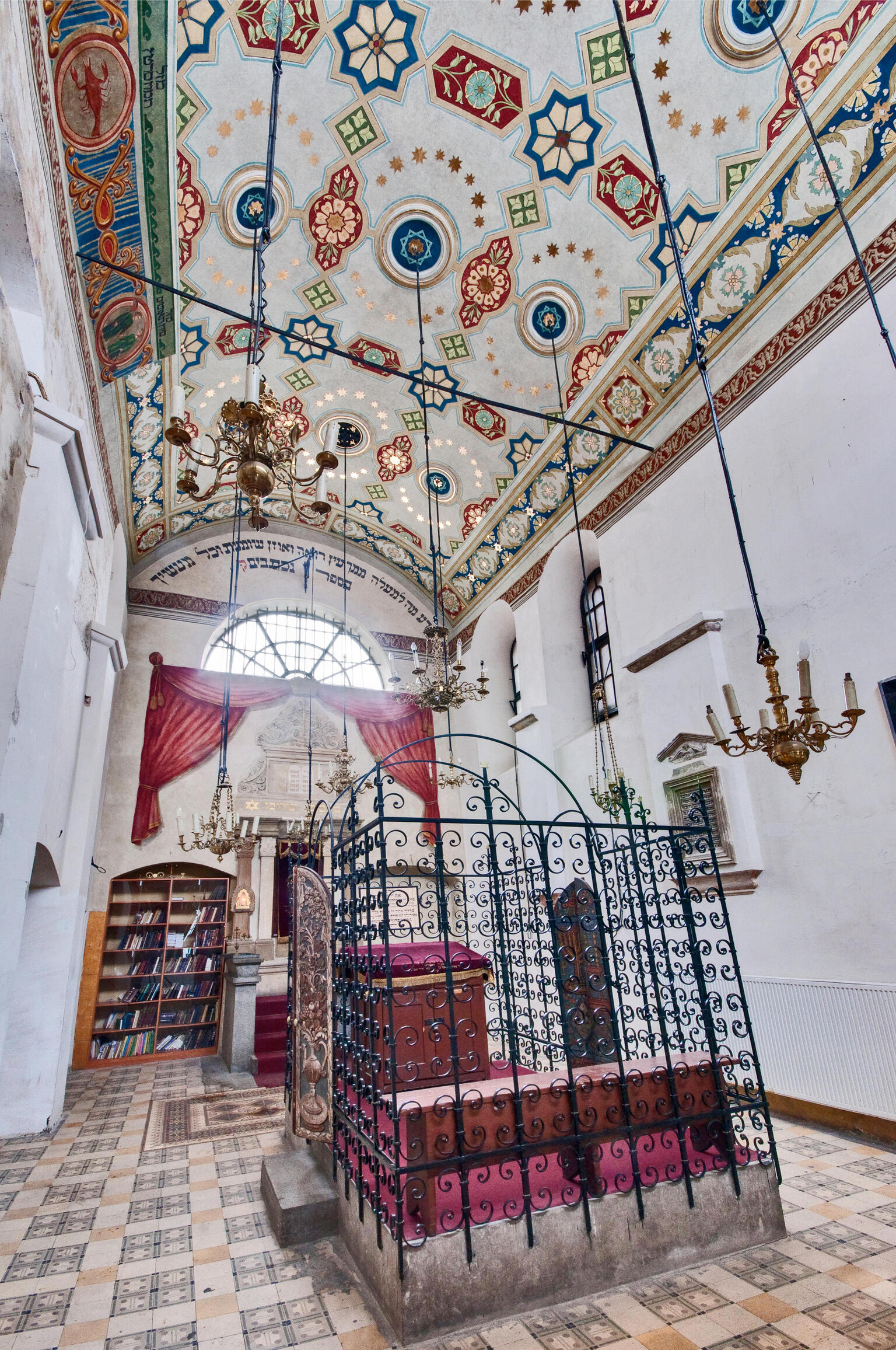 Photograph of room with decorated ceiling, central platform with wrought-iron gate, and bookshelf on far wall.