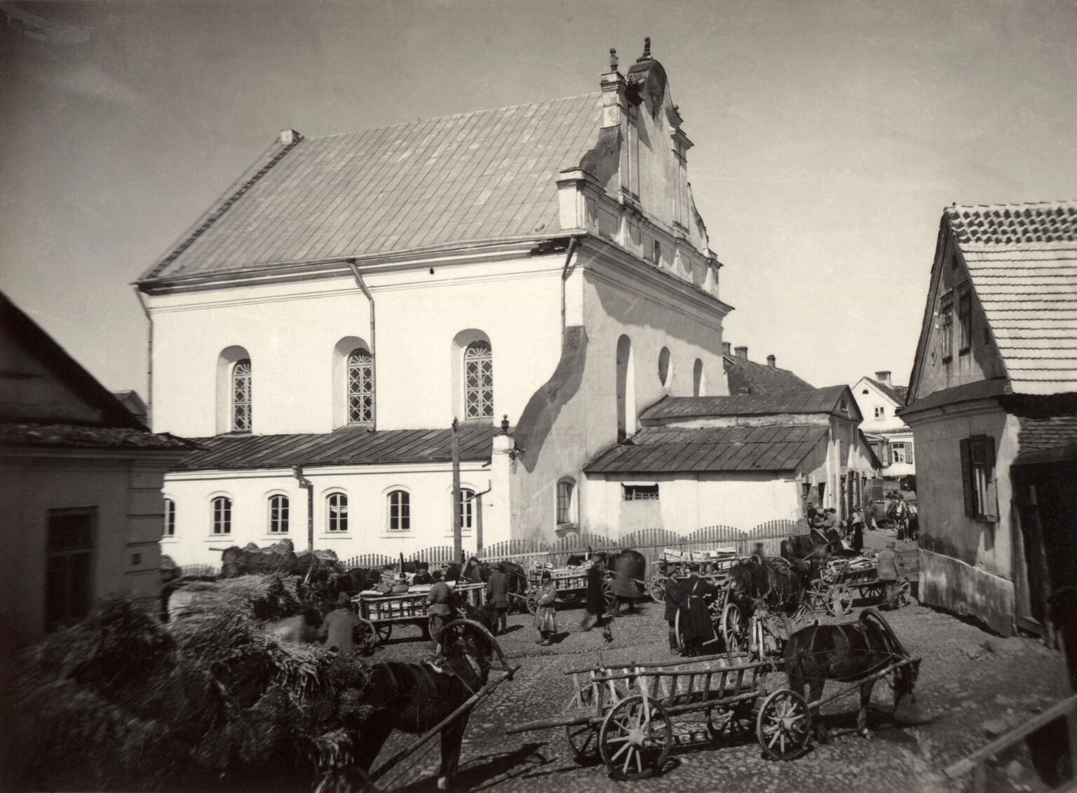 Exterior photograph of buildings on busy street with horses pulling wagons.