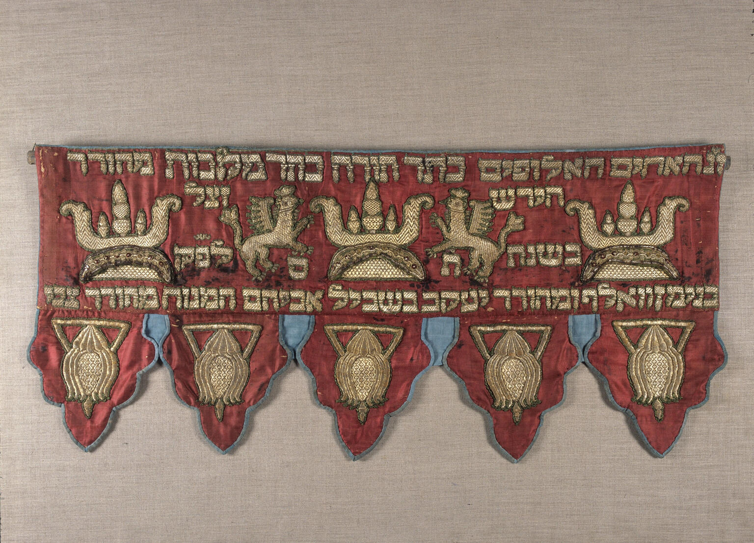 Short curtain embroidered with Hebrew text across the top with griffins and crowns. 