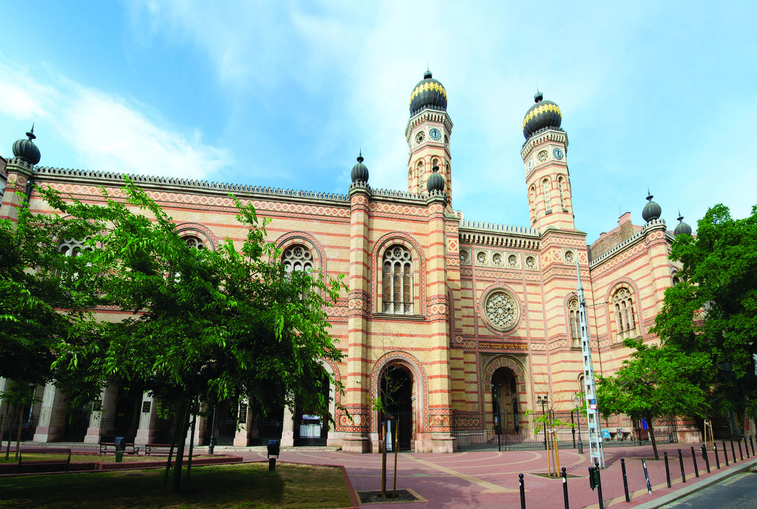Photograph of exterior facade of building with minarets, circular windows, and decoration, and trees in courtyard. Photograph of exterior facade of building with minarets, circular windows, and decoration, and trees in courtyard.