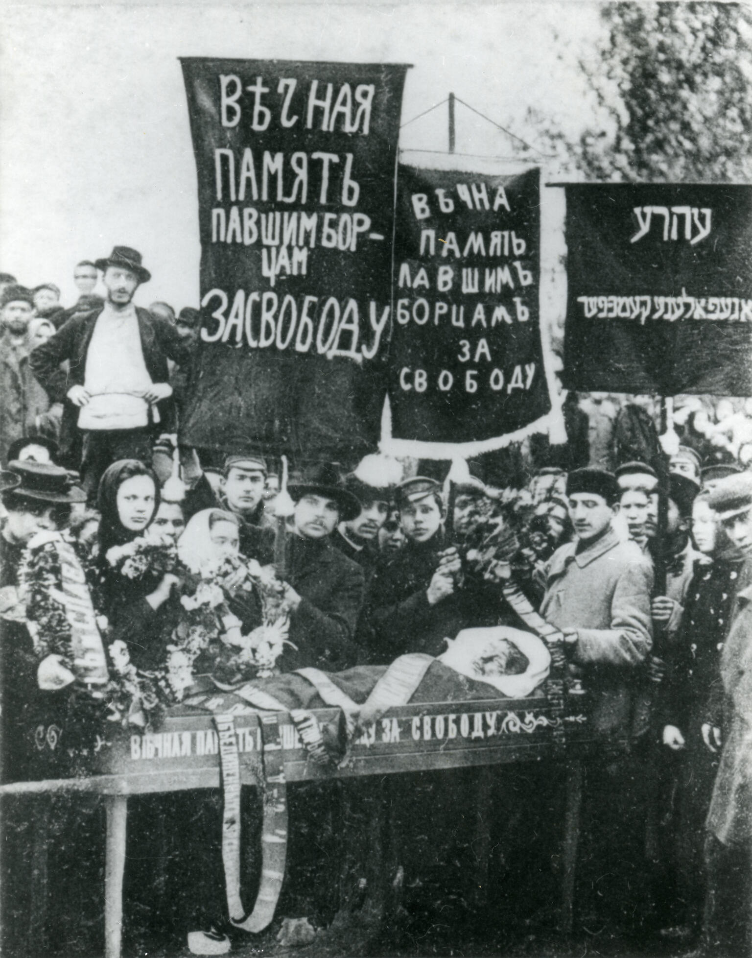 Photograph of crowd of people holding banners in Russian and Yiddish above a coffin. Photograph of crowd of people holding banners in Russian and Yiddish above a coffin.