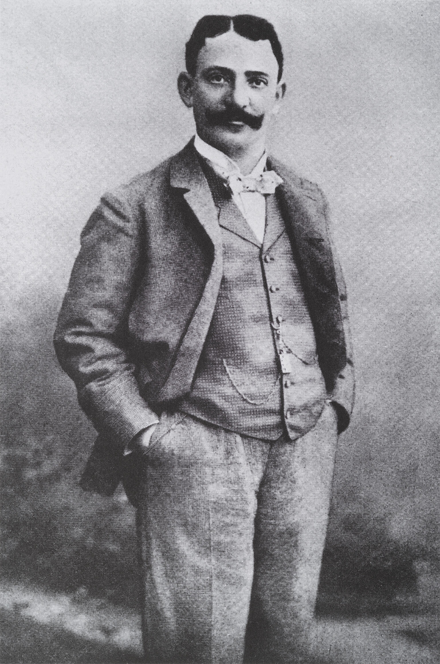 Photograph of man standing with hands in his pockets.