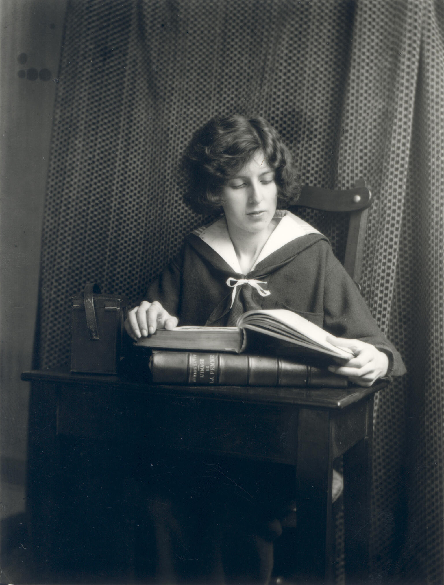 Photograph of figure seated at desk reading a book.