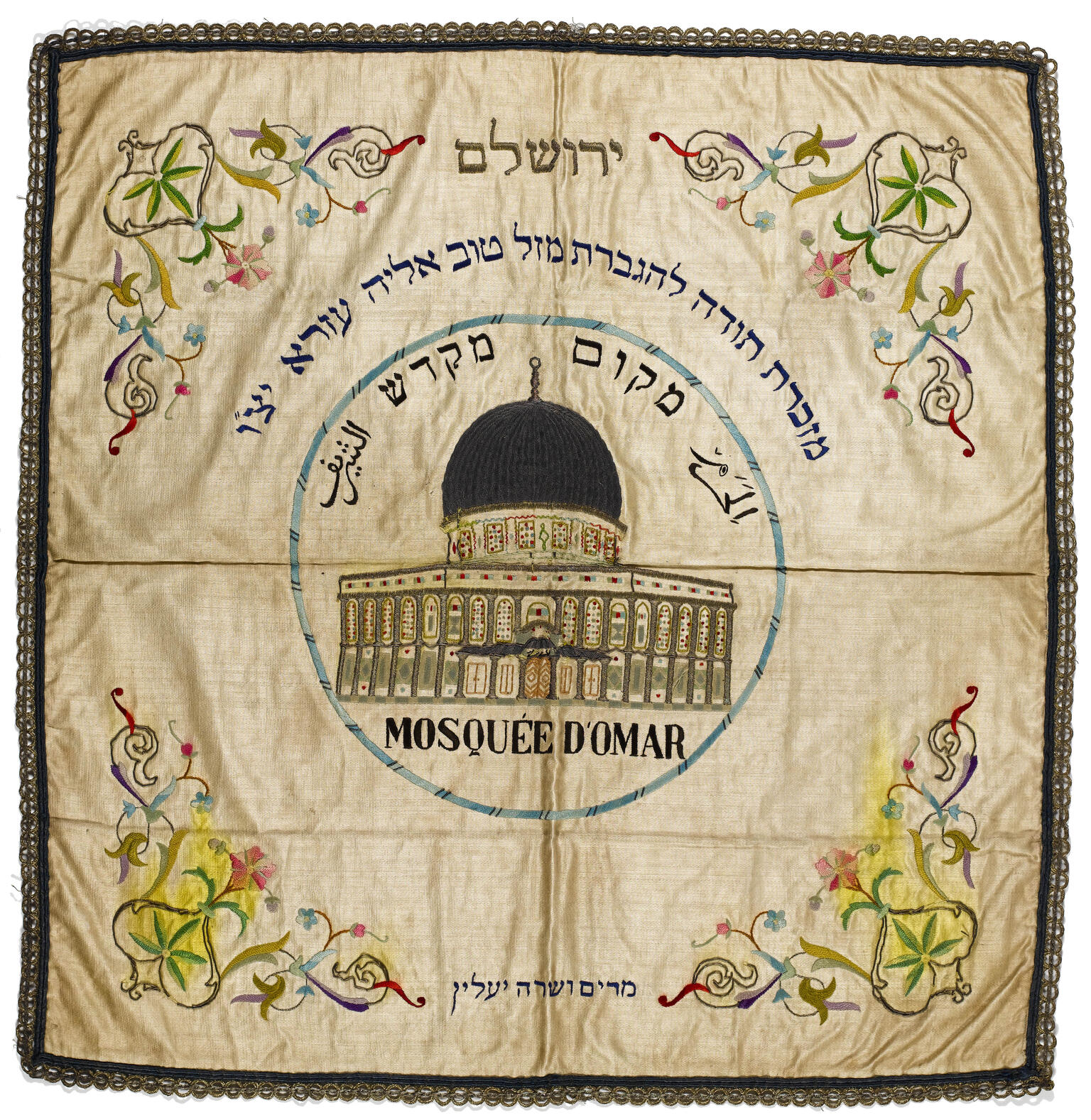 Embroided cloth with domed building in center, surrounded by Hebrew and Arabic text, and flowers in each corner.