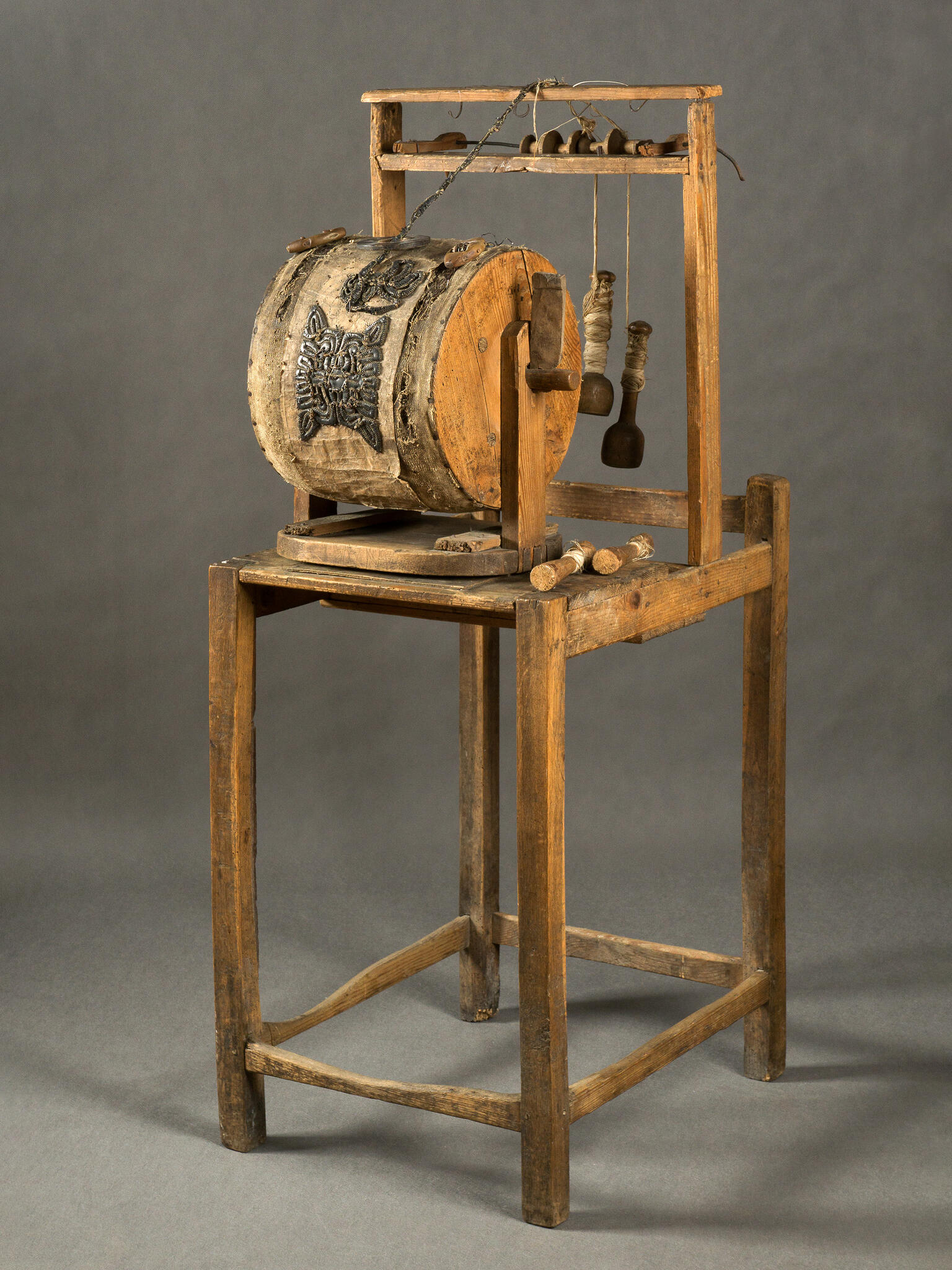 Wooden machine on four legs, with barrel and handle in center.