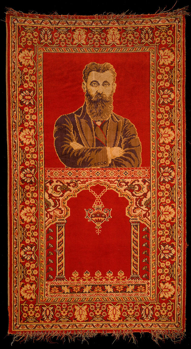 Rug depicting a bearded man with crossed arms on top half, and two columns and hanging lamp on bottom half, surrounded by decorative border.