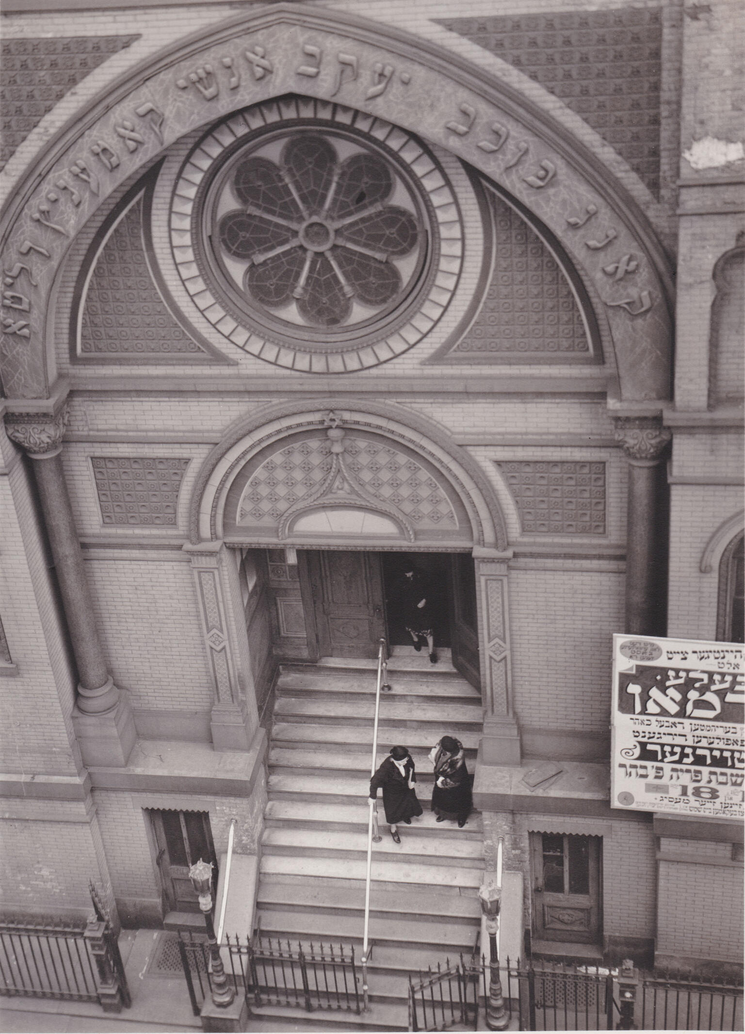 Photograph of building entrance with rose-shaped window and Hebrew inscription seen from above. Photograph of building entrance with rose-shaped window and Hebrew inscription seen from above.