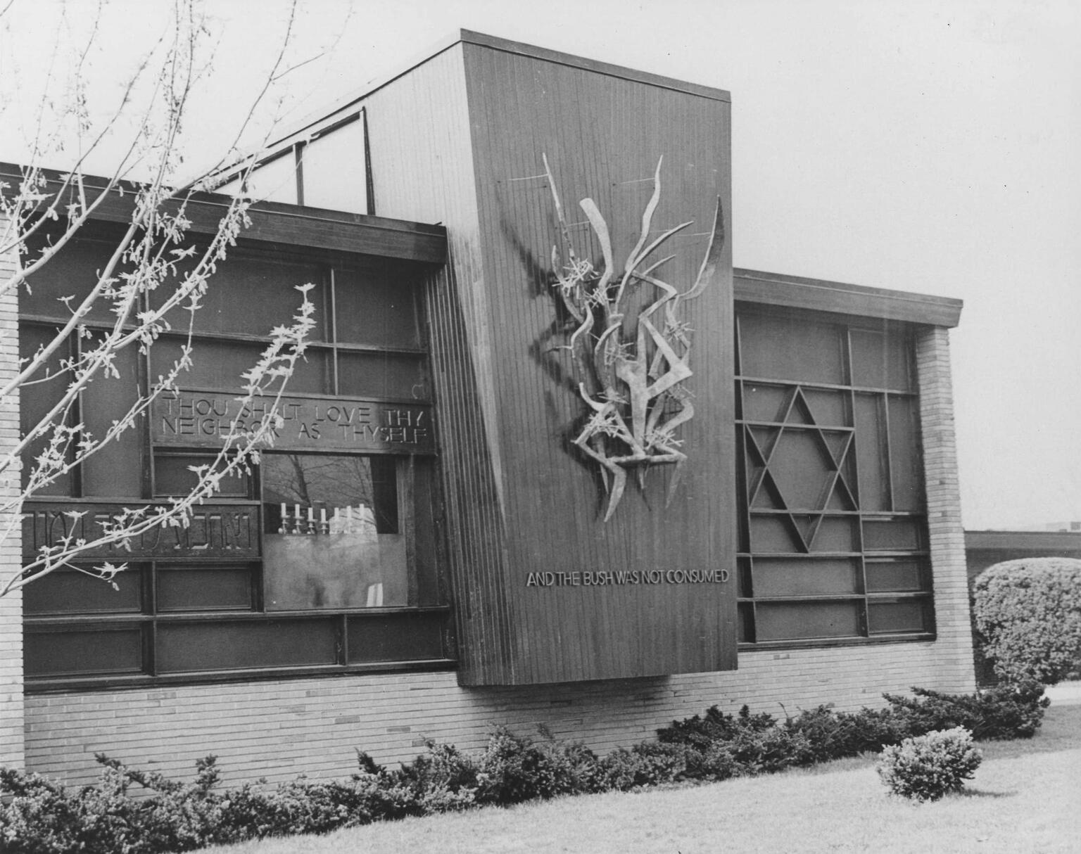 Exterior wall of synagogue featuring Star of David on the right side of the wall and a ribbon-like sculpture in the middle of the wall on a prominent vertical section that juts out from the rest of the wall, with inscription in English reading "And the bush was not consumed." Exterior wall of synagogue featuring Star of David on the right side of the wall and a ribbon-like sculpture in the middle of the wall on a prominent vertical section that juts out from the rest of the wall, with inscription in English reading "And the bush was not consumed."