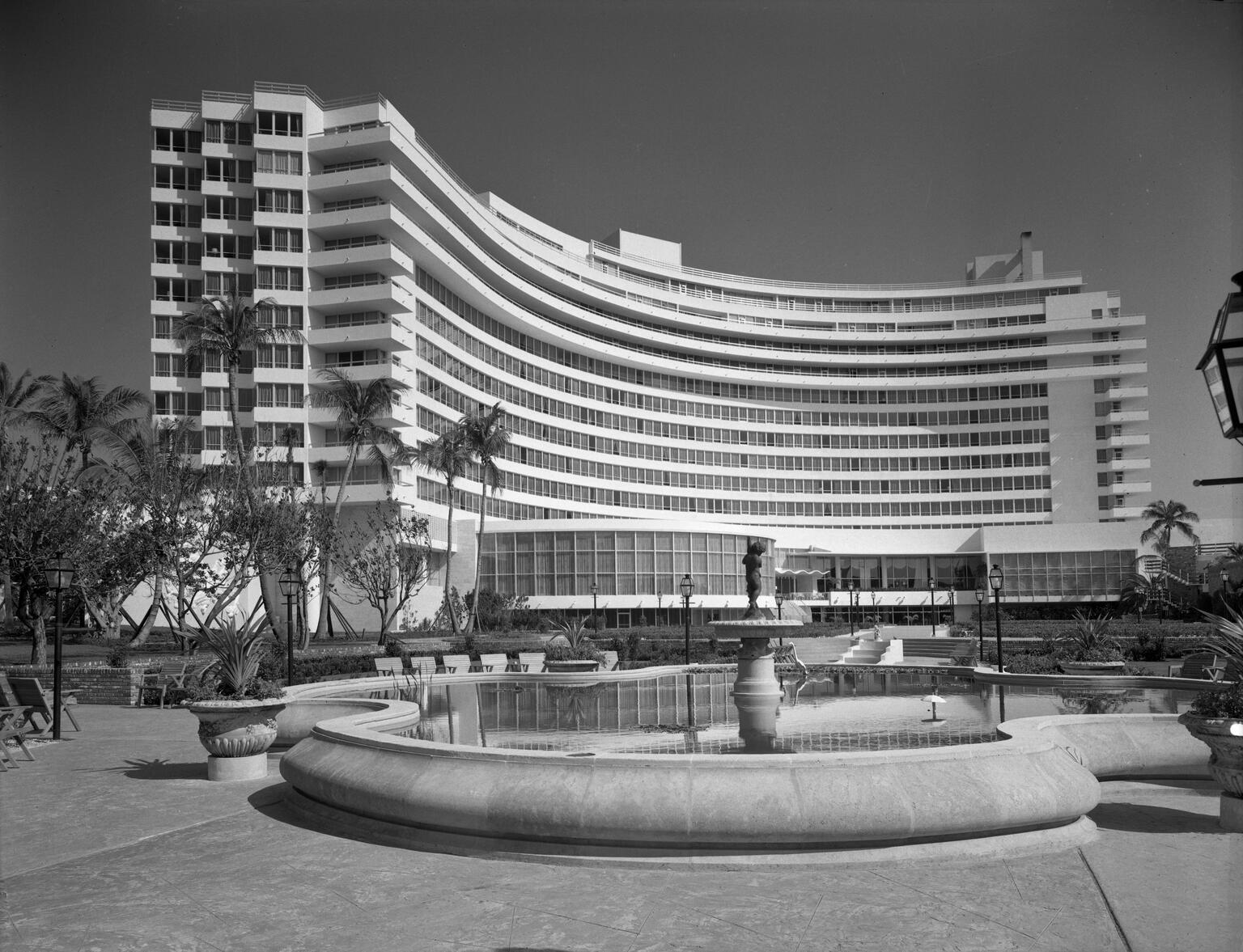 Photograph of curved exterior of a hotel with pool and fountain in the middle. Photograph of curved exterior of a hotel with pool and fountain in the middle.