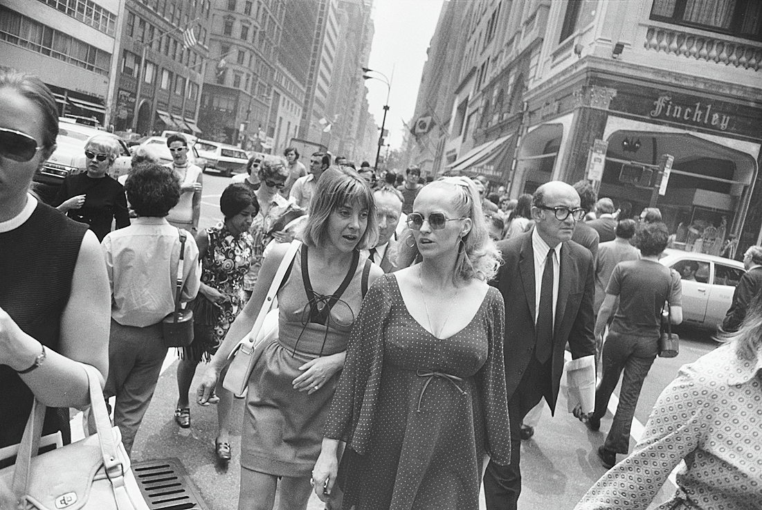 Photograph of two women walking down busy city street toward photographer. 