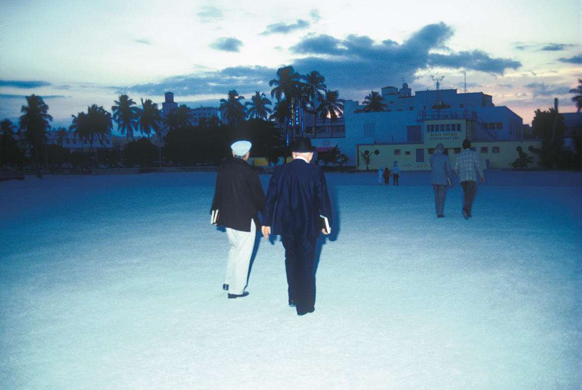 Photograph depicting people walking toward buildings, away from the camera. 