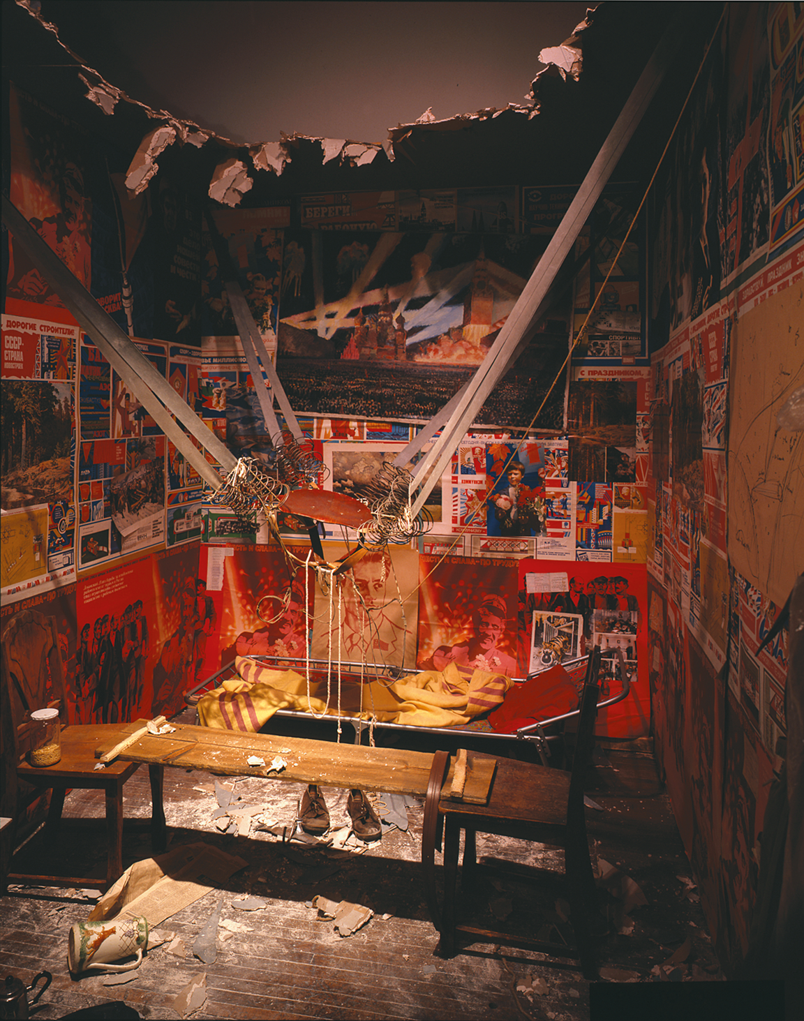 Installation featuring catapult-like contraption in the middle strung between two walls, a hole in the ceiling, and scientific drawings and posters on the walls. Installation featuring catapult-like contraption in the middle strung between two walls, a hole in the ceiling, and scientific drawings and posters on the walls.