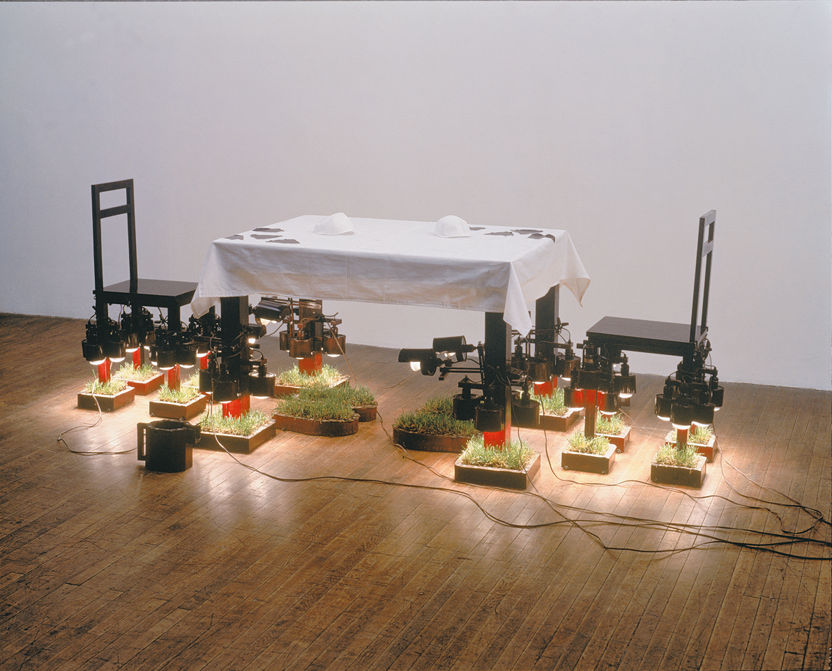 Art installation of table and chairs with individual squares of grass on ground.