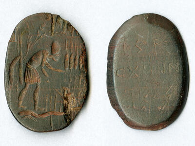 Two views of an ancient engraved oval stone: one side shows a standing, bent-over figure with an arm extended, while the other side displays several lines of inscribed text.