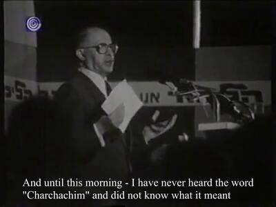 Thumbnail black and white photo of man holding a paper and speaking into microphones on a podium, with Hebrew text behind him in the background and English subtitles below.